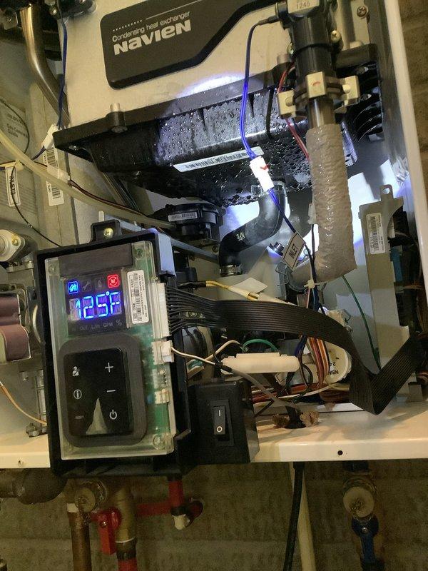 Responded to service call for non-operational tankless water heater system in single-family residence. Upon arrival, inspected dual Navien tankless water heater installation with units mounted side-by-side. Removed front access panels to assess internal components and diagnose malfunction. Observed excessive condensation accumulation on internal black plastic components and housing, indicating potential drainage or ventilation issues. Verified digital display functionality showing temperature reading of 125°F on operational unit. Examined heat exchanger assemblies, burner components, control boards, and circuit systems for both units. Inspected associated plumbing connections including PVC venting, copper supply lines, and isolation valves with proper hot/cold identification. Evaluated electrical connections and wiring integrity throughout both systems. Addressed the reported operational failure and restored system functionality. Documented existing installation configuration and inter