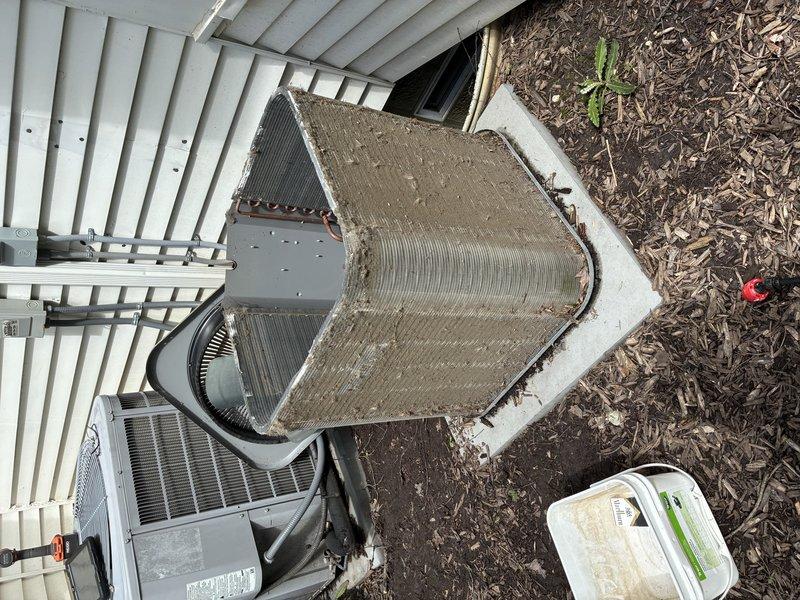 Completed BS-MVP recurring cooling maintenance visit on residential HVAC system. Upon arrival, performed comprehensive inspection of outdoor equipment including triangular A-frame evaporator coil and associated air handler unit. Documented heavy accumulation of dirt, debris, and organic matter on evaporator coil fins, which was significantly restricting airflow and reducing system efficiency. Cleaned and serviced evaporator coil assembly to restore proper heat transfer capability. Inspected flexible ductwork connections and verified proper sealing. Checked concrete pad mounting and equipment positioning. System operational following maintenance procedures.