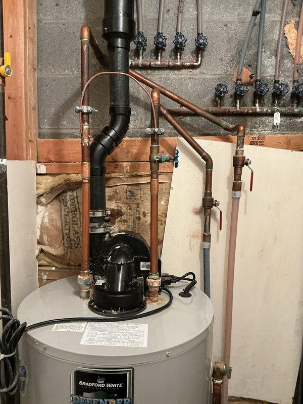 Completed installation of Bradford White tanked water heater system in basement mechanical room. Removed existing water heating equipment and installed new tank-style unit with complete copper supply and discharge piping. Configured PVC drainage system with proper venting and condensate removal connections. Mounted circulation pump assembly on top of water heater tank with appropriate copper pipe connections and isolation valves. Installed manifold distribution system on concrete block wall with multiple shutoff valves for zone control. Ran new copper supply lines with shutoff valves, pressure relief valve, and proper code-compliant connections. Tested all connections for leaks, verified proper pump operation, and ensured adequate drainage flow through PVC waste system. System commissioned and left in full working order.