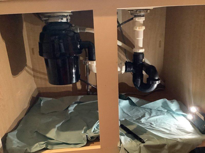 Responded to service call for washing machine drainage issue causing water to back up into kitchen sink. Inspected under-sink plumbing configuration including garbage disposal unit on left side and P-trap assembly on right side. Diagnosed improper drain line connection between washing machine discharge and kitchen sink drain system. Corrected the cross-connection issue to ensure proper drainage separation between appliances, preventing wastewater from washing machine from entering kitchen sink during drain cycles. Verified proper water flow and drainage operation upon completion.