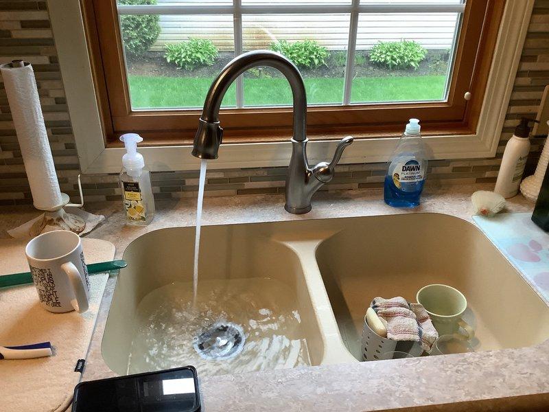 Responded to service call for washing machine drainage issue causing water to back up into kitchen sink. Inspected under-sink plumbing configuration including garbage disposal unit on left side and P-trap assembly on right side. Diagnosed improper drain line connection between washing machine discharge and kitchen sink drain system. Corrected the cross-connection issue to ensure proper drainage separation between appliances, preventing wastewater from washing machine from entering kitchen sink during drain cycles. Verified proper water flow and drainage operation upon completion.