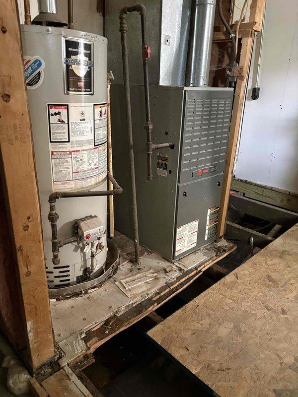 Provided estimate for complete HVAC system replacement including furnace and water heater removal, subfloor leveling and repair, and cold air return replacement in crawl space. Inspection revealed deteriorated crawl space conditions with accumulated debris, damaged ductwork with visible splits in insulation, and compromised flooring in mechanical room requiring structural attention before new equipment installation. Existing gray-green furnace and white cylindrical water heater currently operational but scheduled for removal to allow subfloor restoration and proper equipment placement.