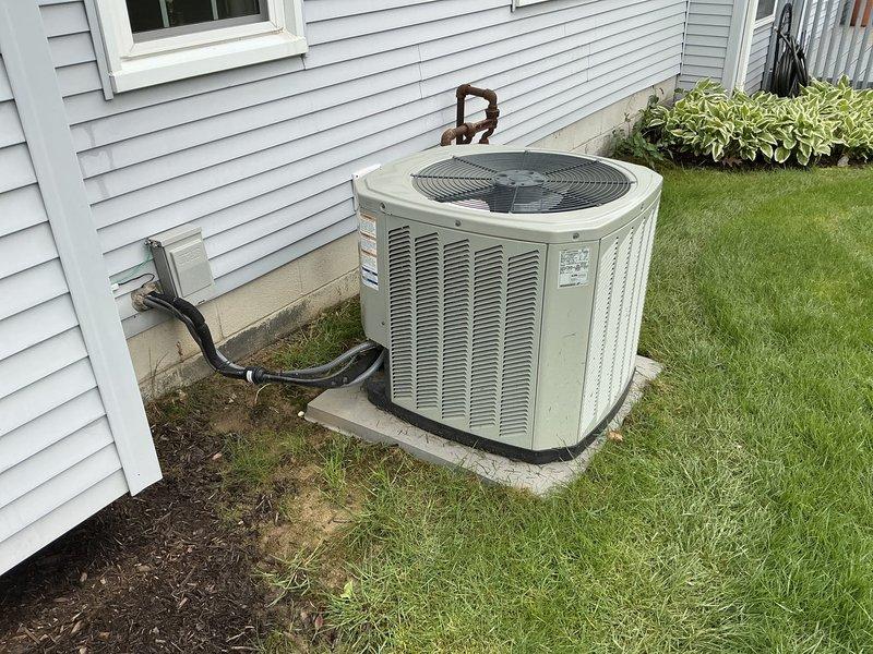 Completed on-site estimate for furnace and air conditioning system replacement. Evaluated existing HVAC system consisting of a beige furnace unit in the basement utility room with galvanized metal ductwork and refrigerant lines, along with an outdoor air conditioning condenser unit positioned on a concrete pad adjacent to the home's exterior. Documented current system configuration including ductwork connections, condensate drain line routing, and refrigerant line penetrations through exterior wall. Photographed both indoor and outdoor equipment to assess replacement requirements and provide accurate equipment sizing recommendations for new system installation.