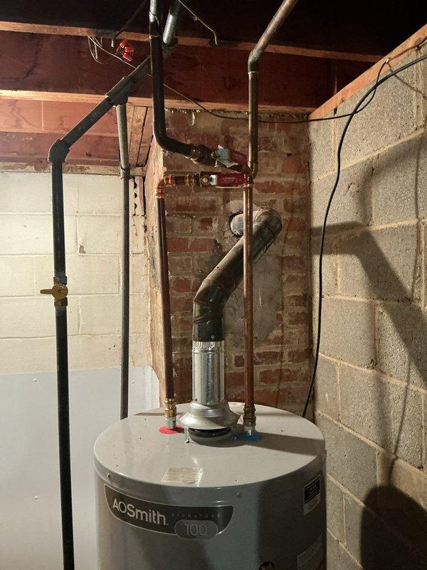 Responded to service call for inoperative hot water heater in 50-year-old residence. Upon arrival, inspected AO Smith 100-gallon tanked water heater located in basement utility area. Unit was not producing hot water as reported. Conducted diagnostic assessment of water heater system, including examination of heating elements, thermostat functionality, gas supply connections, and associated plumbing infrastructure. Evaluated copper and steel piping network, shut-off valves, and pressure relief valve for proper operation. Documented existing installation configuration with exposed brick and concrete block walls in unfinished basement setting. Assessed overall condition of unit and surrounding plumbing connections. Provided technical findings and recommendations to homeowner regarding repair or replacement options based on age and condition of existing equipment.