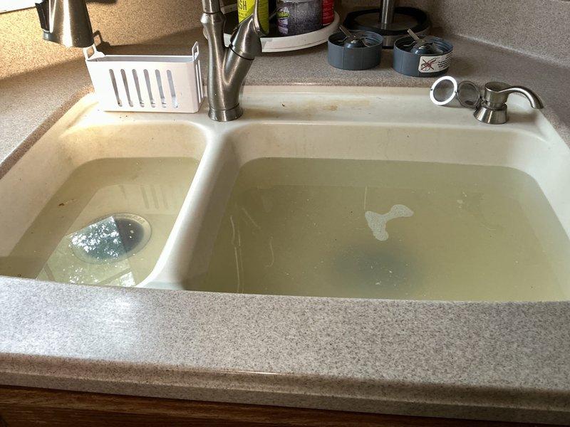 Responded to multiple drain blockages affecting kitchen sink, dishwasher, garbage disposal, and bathroom sink. Upon arrival, found standing water in both basins of kitchen double-basin sink with cloudy, debris-laden water indicating complete drainage failure. Accessed main drain line through basement crawl space and cleared obstruction in primary waste stack. Restored proper drainage to all affected fixtures, verified garbage disposal operation, and confirmed dishwasher drain line was flowing freely.