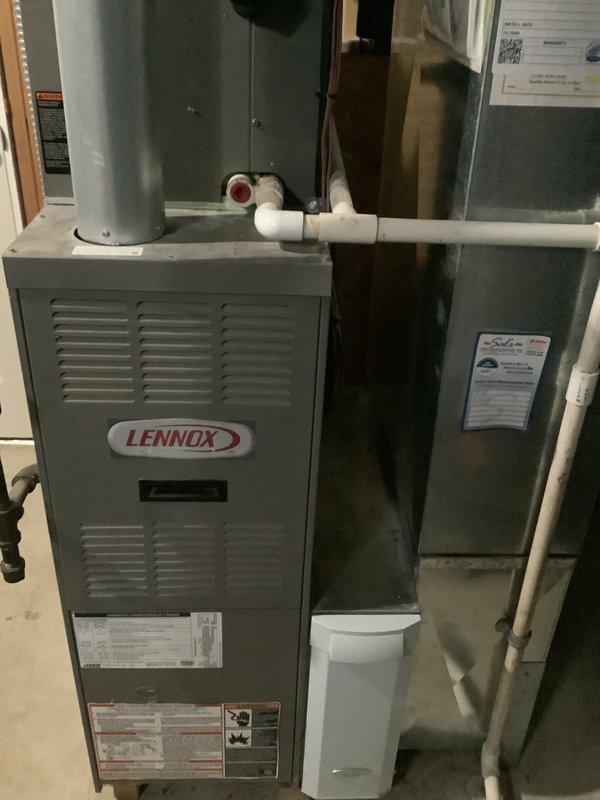 Completed estimate for replacement of residential HVAC system requiring a 2.5 ton capacity unit. Assessed existing Lennox furnace installation in basement utility area, including evaluation of current ductwork configuration, condensate drain lines, and air handler positioning. Documented equipment specifications and existing system layout including water heater proximity and PVC piping connections. Reviewed mechanical room space constraints and structural considerations for new equipment installation. Examined current electrical connections, gas line access, and ventilation requirements. Photographed existing furnace unit with manufacturer labels, air handler mounting, insulation conditions, and associated plumbing connections to support replacement specifications and installation planning.