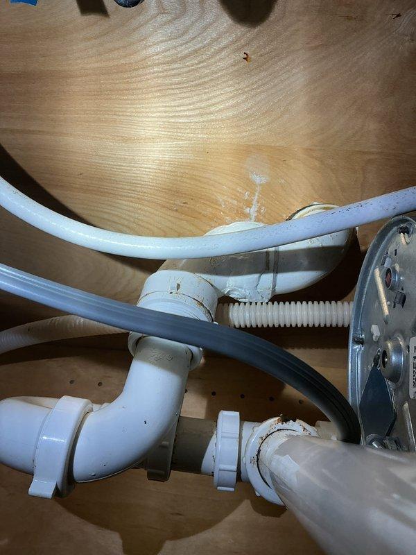 Responded to plumbing leak under kitchen sink in 94-year-old home. Upon arrival, water supply to sink was already shut off by homeowner. Inspected under-sink plumbing assembly including white PVC drain lines, P-trap configuration, garbage disposal unit, and supply connections. Identified source of leak and assessed condition of existing plumbing components. Documented cabinet interior setup with disposal motor unit, mounting hardware, and drain assembly connections. Placed protective cloth and catch container beneath plumbing to prevent water damage during inspection and repair work. Addressed leak issue, verified all connections were secure, and confirmed proper drainage function before restoring water supply to sink.