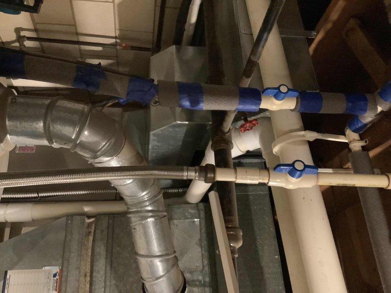 Provided estimate for replacement of water heater over 10 years old. Inspected existing installation including water supply lines with blue-handled ball valves, PVC piping configuration, and flexible stainless steel connectors in utility area. Documented current equipment condition and mechanical room layout for water heater replacement quote.