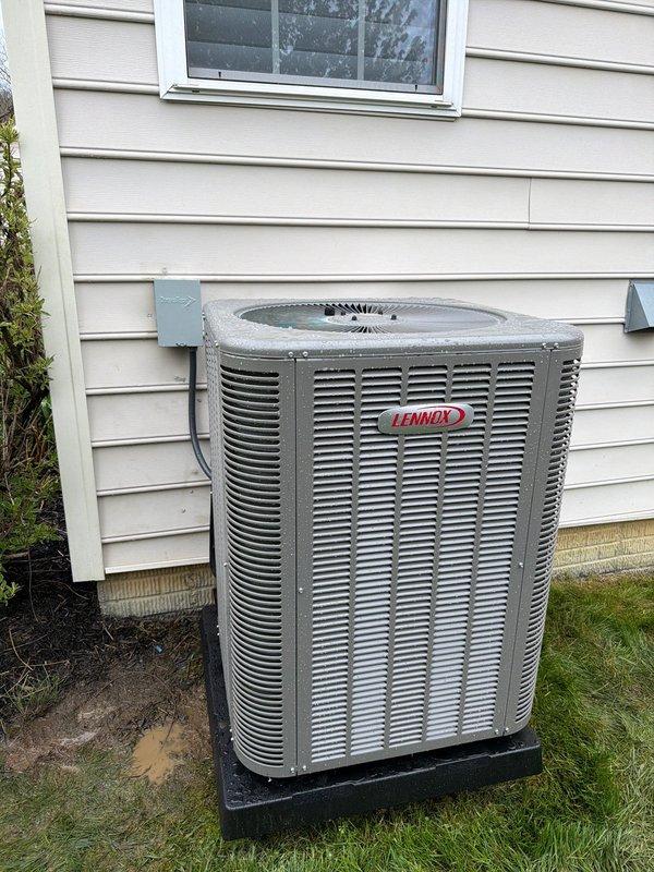 Completed installation of 80% AFUE furnace and air conditioning system at residential property. Installed new Lennox outdoor condensing unit on rubber isolation pad against exterior wall with proper clearances maintained. Unit positioned on level pad with electrical disconnect box mounted to building exterior and refrigerant line set routed through wall penetration. Installed new fuse block assembly with appropriately rated FLNR and FRE30R fuses for overcurrent protection of equipment. Connected copper wiring to fuse block terminals and secured all electrical connections per manufacturer specifications and local electrical codes. Routed electrical conduit along exterior siding to disconnect box. Verified proper grounding of all components. System installation completed in damp weather conditions. All equipment secured and operational.