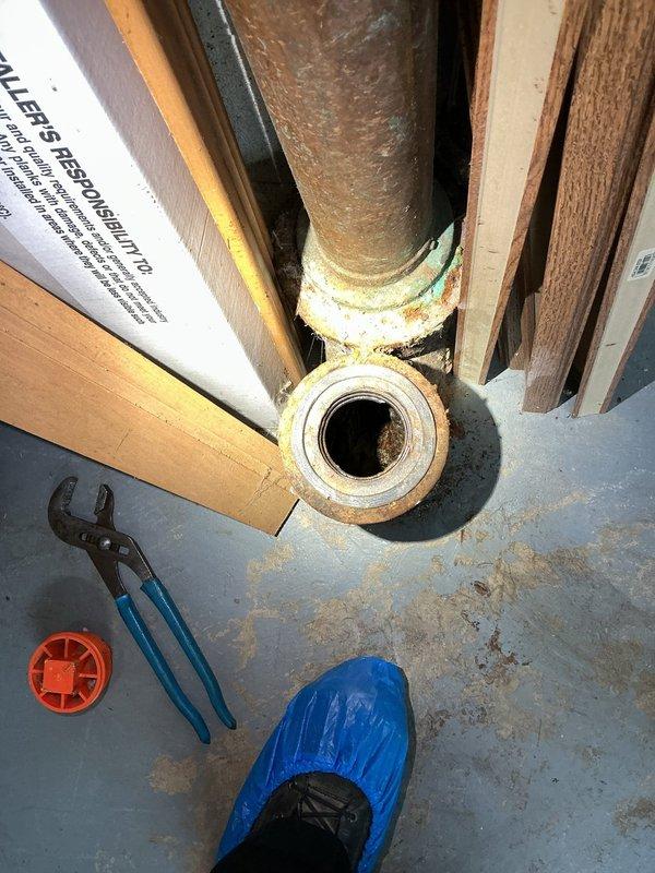 Responded to main drain backup in basement. Upon arrival, located the main drain cleanout access point near vertical stack penetrating floor structure. Evidence of active drainage issues was visible with significant water staining and discoloration on concrete floor surrounding drain area. Assessed PVC drain line connection and black flexible drainage components for blockages and flow restrictions. Performed drain cleanout procedure to clear obstruction in main line. Verified proper drainage flow restored through system. Documented existing corrosion on metal flange at pipe penetration point and moisture damage to surrounding floor area for customer awareness.