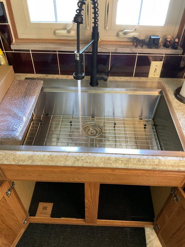 Removed existing stainless steel kitchen sink and installed customer-supplied undermount stainless steel sink with protective grid rack into granite countertop. Installed new black matte finish pull-down kitchen faucet with spray head. Connected all plumbing components including P-trap assembly to existing garbage disposal unit, verified proper drainage, and tested all connections for leaks.