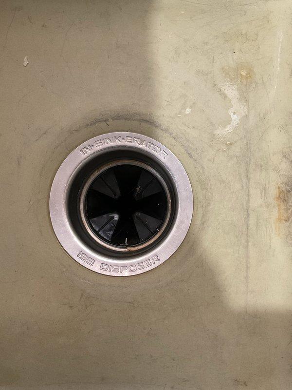 Responded to service call for non-functioning outdoor spigots and leaking garbage disposal. Inspected front and rear exterior hose bibs, confirming rear spigot supply line was disconnected during previous bathroom remodel and front spigot required repair due to failed internal components. Evaluated InSinkErator garbage disposal unit and identified active leak at mounting flange or drain connection. Documented existing conditions with photographs of disposal unit from above showing wear patterns and exterior utility area near foundation. Provided assessment of required repairs including potential supply line restoration for rear spigot, component replacement or installation for front spigot, and disposal leak remediation through gasket replacement or unit resealing.