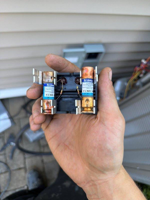 Completed installation of downflow air conditioning system at residential property. Installed outdoor condensing unit on paver patio with proper electrical disconnect and conduit routing, positioned unit against exterior wall with adequate clearance for airflow and maintenance access. Replaced damaged fuse block assembly that showed signs of heat exposure, installed new dual-fuse protection with proper amperage rating to ensure safe electrical operation of the system.