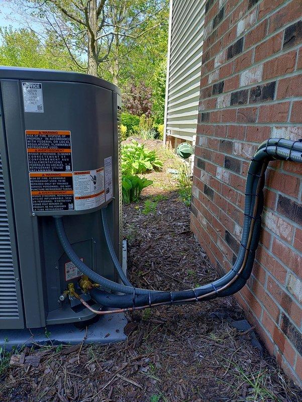 # HVAC Install - Complete System

Completed installation of complete HVAC system including outdoor condensing unit and associated components. Positioned air conditioning condenser unit in side yard access area between residence exterior and property line. Installed refrigerant line set with proper insulation, routing lines from outdoor unit through brick wall penetration into conditioned space. Secured black corrugated conduit along exterior brick wall and around building corner for line set protection. Mounted electrical disconnect box on vinyl siding near unit location to meet code requirements. Verified proper clearances around outdoor equipment for adequate airflow and future serviceability. System tested and operational upon completion.