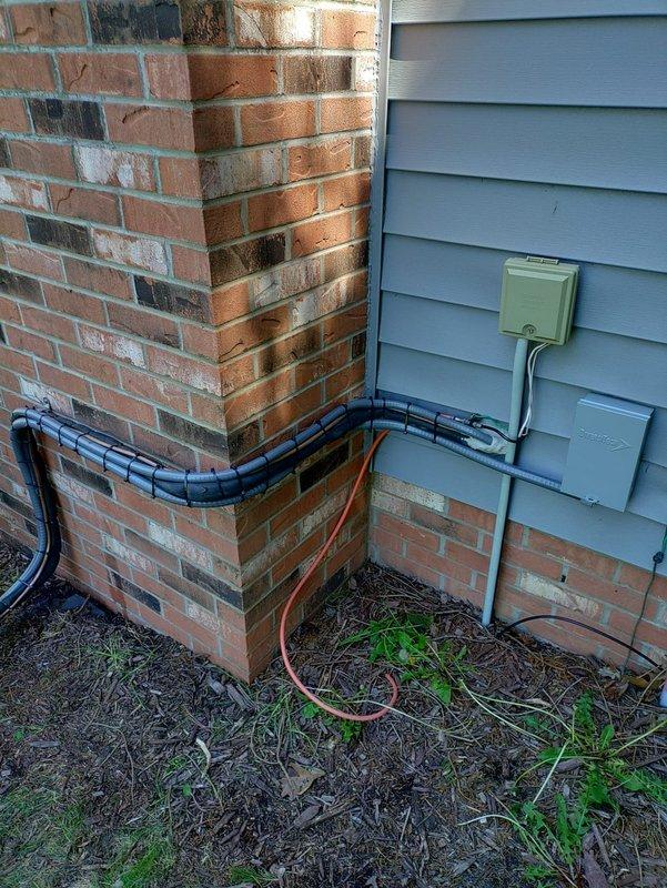 # HVAC Install - Complete System

Completed installation of complete HVAC system including outdoor condensing unit and associated components. Positioned air conditioning condenser unit in side yard access area between residence exterior and property line. Installed refrigerant line set with proper insulation, routing lines from outdoor unit through brick wall penetration into conditioned space. Secured black corrugated conduit along exterior brick wall and around building corner for line set protection. Mounted electrical disconnect box on vinyl siding near unit location to meet code requirements. Verified proper clearances around outdoor equipment for adequate airflow and future serviceability. System tested and operational upon completion.