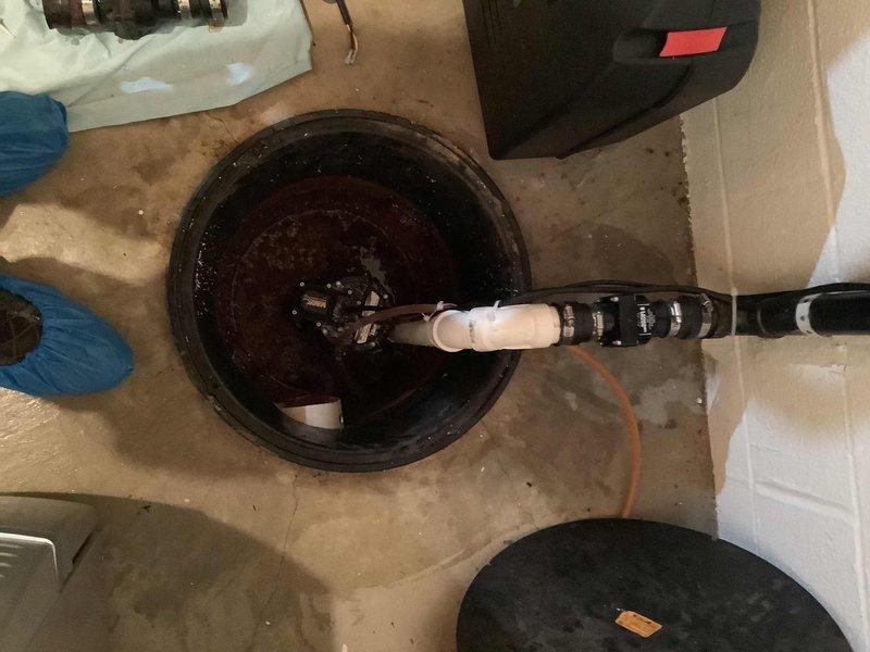 Responded to service call for sump pump failure where unit was not triggering properly. Upon inspection, found submersible pump installed in basement floor basin with standing water present. Evaluated pump operation, electrical connections, and float switch mechanism to diagnose triggering issue. Assessed pump components including motor assembly and discharge system, documented existing conditions with basin cover removed, and verified power supply routing from wall-mounted junction box to pump unit. Recommended repair or replacement options based on operational assessment findings.
