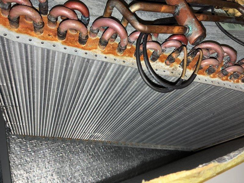 Completed preventive maintenance cooling visit on 9-year-old air conditioning system. Performed standard inspection of evaporator coil assembly and ductwork components in attic space. Documented significant rust and corrosion present on coil mounting header and refrigerant tube connection points, indicating extended moisture exposure. Copper refrigerant lines showing oxidation and patina formation. System remains operational following maintenance service. Photographic documentation captured for service records showing condition of finned coil assembly, corroded mounting plate, and insulated ductwork connections.