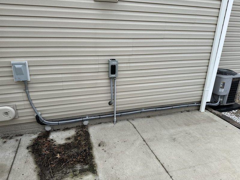 Relocated existing air conditioning condenser unit to the right side of the building exterior. Unit was repositioned on a new composite pad with proper gravel base for drainage and stability, with electrical conduit rerouted along the vinyl siding to accommodate the new placement.