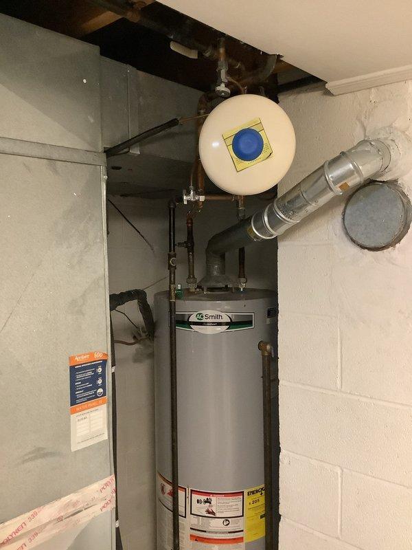 Responded to customer complaint of continued noise from tanked water heater following recent flush service. Upon inspection, observed AO Smith water heater installation with copper supply piping, expansion tank, and proper venting system in place. Examined all plumbing connections, valves, and water meter assembly for potential sources of noise generation. Assessed condition of aging copper piping showing surface corrosion and patina buildup. Documented water heater configuration including electrical panel proximity and exhaust vent routing. Investigation focused on identifying cause of persistent operational noise that began after previous maintenance visit.