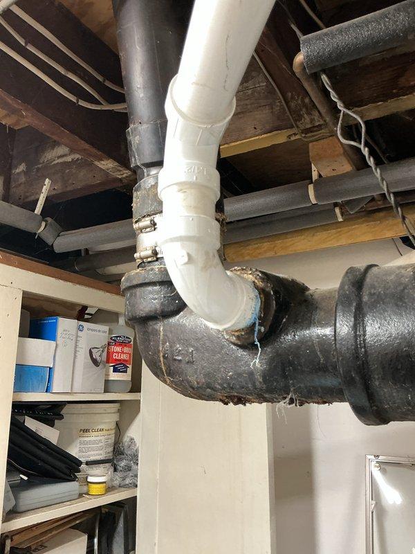 Responded to a leaking PVC glue fitting under the kitchen sink that had been temporarily patched with JB Weld. Completely rebuilt the kitchen drain system starting from the cast iron pipe connection in the basement. Corrected improper drainage pitch and relocated the drain line to the left rear corner of the cabinet. Drilled new access hole through cabinet base for proper routing. Installed new garbage disposal with complete trap assembly, end outlet waste, and air admittance valve. Capped both the male adapter connection under the sink and the original basement drop point with Fernco caps to seal abandoned sections. Replaced both straight stop shut-off valves under the sink with updated fixtures to ensure reliable water supply control and prevent future leaks.