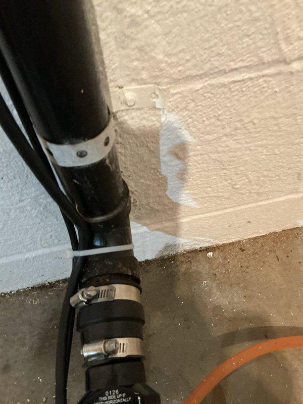 Responded to callback for leak at sump pump discharge piping following recent pump replacement. Upon inspection, identified active moisture and water staining on wall near elbow connection of vertical discharge pipe. Verified leak source at pipe fitting, tightened connection, and confirmed proper mounting bracket placement to prevent future stress on joints.