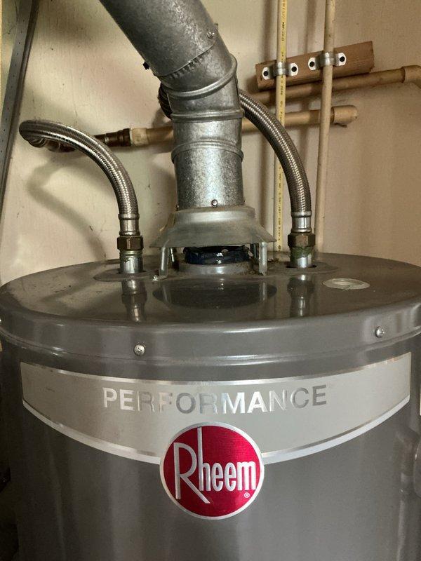 Responded to water leak at top of residential water heater. Upon inspection, identified a 40-gallon Rheem Performance natural gas water heater (Model YE40T06ET-58U1) manufactured in November 2019. Examined top connections including temperature/pressure relief valve, cold water inlet with braided stainless steel connector, and hot water outlet assembly. Documented existing plumbing configuration with copper supply lines and galvanized piping. Assessed leak source at upper tank connections and provided recommendations for repair or replacement based on findings.