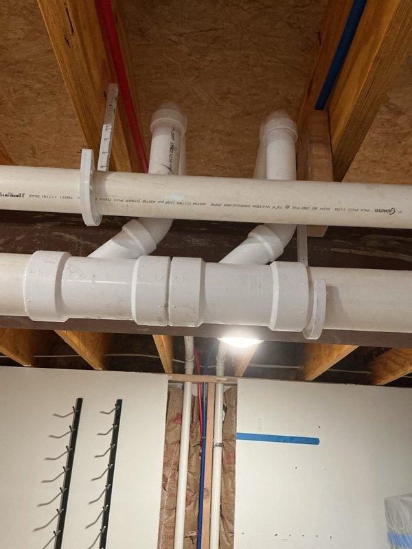 Installed sink pump with complete drainage system including new PVC drain and vent lines routed through ceiling joists and wall cavities. Roughed in hot and cold water supply lines using copper piping, establishing proper connections to the pump assembly. All plumbing lines were secured and positioned in accordance with code requirements, with protective coverings maintained throughout the work area to prevent damage to surrounding surfaces.