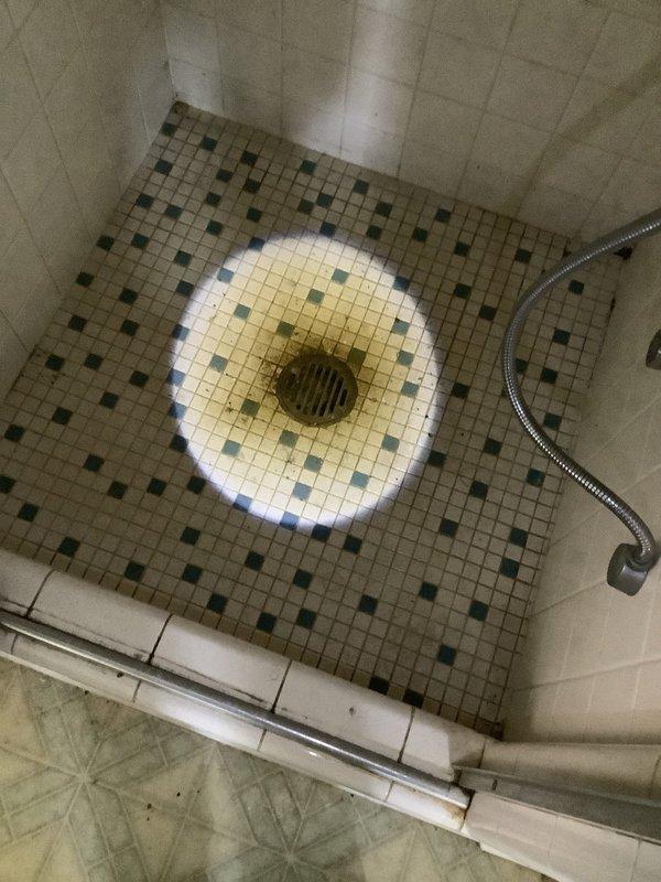 Responded to recurring drainage backup affecting toilet and shower in 40-year-old residence. Accessed plumbing system through floor cavity, exposing PVC drain lines with multiple elbows and connections between fixtures. Cleared obstruction in main drainage line causing backup from toilet to shower area. Inspected vintage mosaic tile shower floor with center drain and verified proper flow restoration. Due to the age of the plumbing system and recurring nature of the blockage, recommended monitoring for potential underlying issues with drain line integrity or pitch that may require future attention.