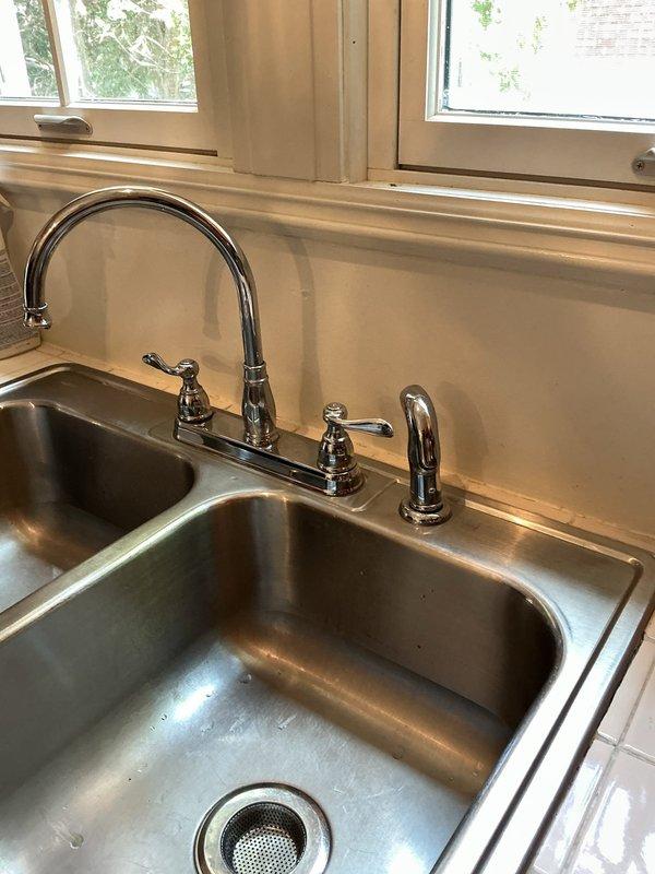 Completed installation of customer-supplied kitchen faucet with high-arched spout and separate spray nozzle in double-basin stainless steel sink. Repaired leaking outdoor hose bib at exterior brick wall foundation, restoring proper function and eliminating water waste.