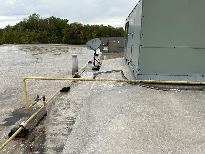 Conducted commercial HVAC replacement estimate for rooftop unit and mini split system. Assessed existing light green rooftop package unit showing significant weathering, water staining, and rust at base mounting points. Evaluated roof access conditions and confirmed ladder not required for future installation. Inspected IT room mini split location and documented rooftop infrastructure including electrical conduit routing and existing mechanical equipment layout for replacement planning.