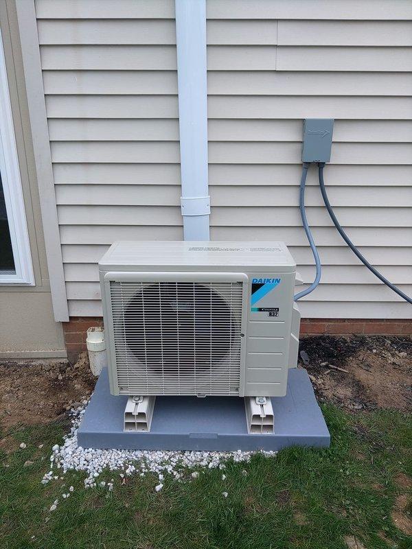 Completed installation of a single-head Daikin ductless mini-split system. Mounted outdoor condenser unit on elevated pad with proper support blocks against exterior wall, installed indoor wall-mounted air handler near ceiling, and ran refrigerant lines with proper insulation from condenser to indoor unit. System tested and operational upon completion.