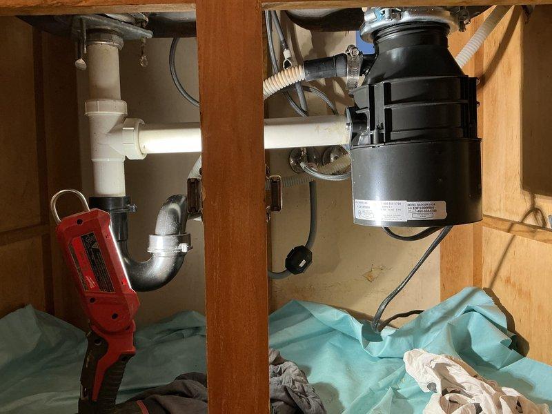 Responded to active water leak under kitchen sink in 55-year-old residence. Upon inspection, identified leak source at garbage disposal unit and associated drain connections. Examined all plumbing components including PVC drain assembly, P-trap configuration, and disposal mounting hardware. Documented existing conditions with photographs showing garbage disposal unit, drain piping, and cabinet interior. Assessed electrical connections and verified proper installation of disposal unit and related plumbing fixtures to determine repair requirements.