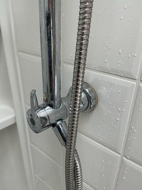 Responded to service call for toilet leak causing water damage to ceiling below. Upon inspection, discovered leak was originating from shower system rather than toilet. Inspected dual shower head assembly with handheld unit and adjustable slide bar mounted on subway tile wall. Identified compromised connection points at chrome fixtures where water was bypassing seals and penetrating wall cavity. Documented existing moisture on tile surfaces and fixtures. Recommended repair of shower valve connections and potential assessment of wall cavity damage to prevent further water intrusion to lower level ceiling.