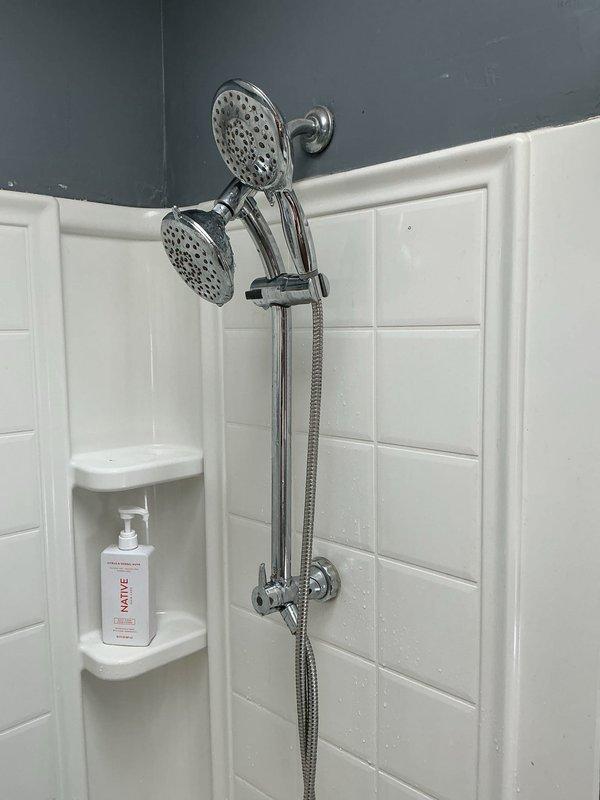 Responded to service call for toilet leak causing water damage to ceiling below. Upon inspection, discovered leak was originating from shower system rather than toilet. Inspected dual shower head assembly with handheld unit and adjustable slide bar mounted on subway tile wall. Identified compromised connection points at chrome fixtures where water was bypassing seals and penetrating wall cavity. Documented existing moisture on tile surfaces and fixtures. Recommended repair of shower valve connections and potential assessment of wall cavity damage to prevent further water intrusion to lower level ceiling.