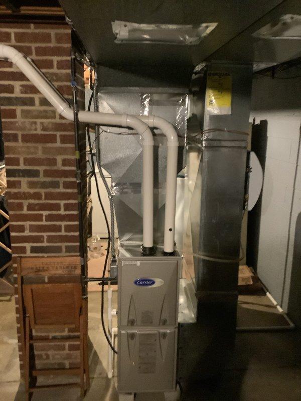 Completed installation of new air conditioning system including outdoor condensing unit and indoor evaporator coil. Outdoor unit was positioned on mulch bed against brick exterior wall with proper clearances maintained, electrical disconnect box mounted to building, and line set connected through foundation. Indoor evaporator coil was installed in conjunction with existing Carrier furnace in basement mechanical room, with refrigerant lines properly insulated and routed. System was vacuum tested, charged to manufacturer specifications, and operationally verified with all electrical connections completed per code requirements.