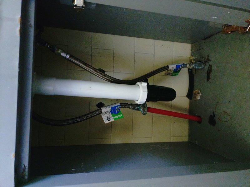 Responded to service call for upstairs bathroom faucet leak at the water shut-off valve and slow-draining sink. Upon inspection, accessed the under-sink cabinet and examined the supply line connections, P-trap assembly, and drain components. Identified leak source at the supply valve connection and assessed the drain system for blockages or improper venting causing the drainage issue. Photographed the existing plumbing configuration, including the water filtration system, braided supply lines, and drain assembly for documentation purposes.