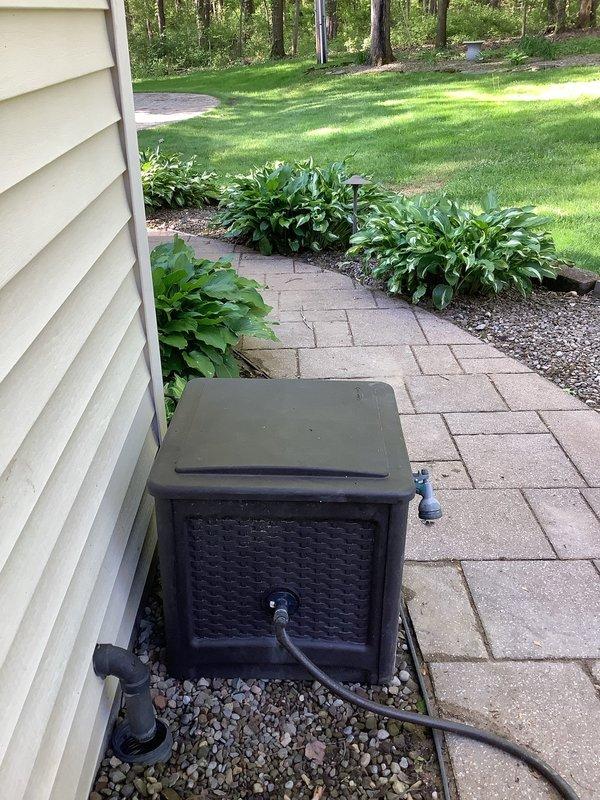 Performed video camera inspection of exterior sump pump discharge line located at southwest corner of residence near garage. Black corrugated pipe was experiencing backup and overflow issues during heavy rainfall events. Camera investigation confirmed discharge line condition and verified connection point to downspout drainage system. Documented findings with photographic evidence of utility box installation on gravel bed adjacent to house foundation and drainage components near entrance area. Inspection completed to determine necessary repairs, with recommendations provided based on camera footage results.