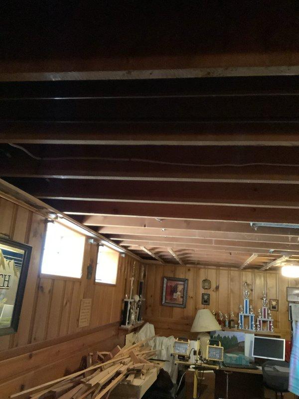 Performed diagnostic evaluation of basement lighting configuration to assess feasibility of relocating two existing light fixtures. Inspected ceiling structure, including exposed wooden joists and existing electrical rough-in, and documented current fixture placement in finished lower level with wood-paneled walls. Examined accessible ceiling cavity through opened section revealing HVAC ductwork and electrical wiring pathways. Evaluated structural limitations, existing switch locations on knotty pine paneling, and available routing options for new fixture placement. Provided customer with multiple relocation options based on ceiling joist spacing, ductwork clearances, and electrical code requirements for future installation work.
