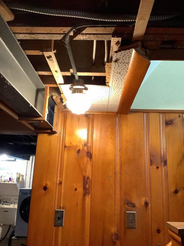 Performed diagnostic evaluation of basement lighting configuration to assess feasibility of relocating two existing light fixtures. Inspected ceiling structure, including exposed wooden joists and existing electrical rough-in, and documented current fixture placement in finished lower level with wood-paneled walls. Examined accessible ceiling cavity through opened section revealing HVAC ductwork and electrical wiring pathways. Evaluated structural limitations, existing switch locations on knotty pine paneling, and available routing options for new fixture placement. Provided customer with multiple relocation options based on ceiling joist spacing, ductwork clearances, and electrical code requirements for future installation work.