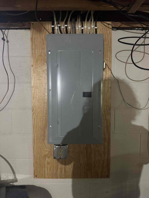 Completed 200 amp electrical service upgrade in residential basement, installing new main circuit breaker panel mounted on plywood backing board with proper conduit entry from above. Installed dedicated circuit for tankless water heater system as part of the service upgrade. Added convenience duplex receptacle outlet below main panel for utility access, with all wiring properly secured and routed through conduit per code requirements.