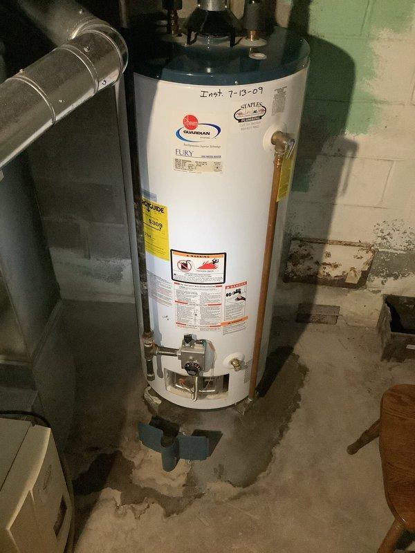 Performed no-cost estimate for replacement of 19-year-old gas water heater exhibiting active leak from tank bottom. Upon inspection, confirmed water damage on concrete floor surrounding unit base and verified installation date of July 2007 from tank markings. Assessed existing plumbing connections, pressure relief valve, gas supply line, and venting system to determine replacement requirements and specifications for new water heater installation.