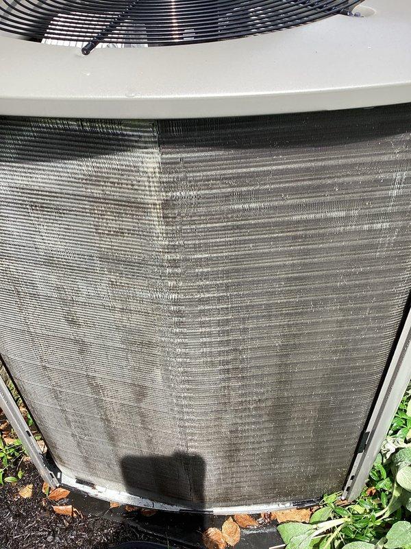 Completed routine maintenance visit on a 2-year-old residential air conditioning system for MVP customer. Upon inspection, found significant accumulation of dirt, dust, and debris on the outdoor condenser coil fins and protective grille, which can restrict airflow and reduce system efficiency. Documented unit condition with photographs showing the extent of contamination on both the heat exchanger panel and exterior mesh components.