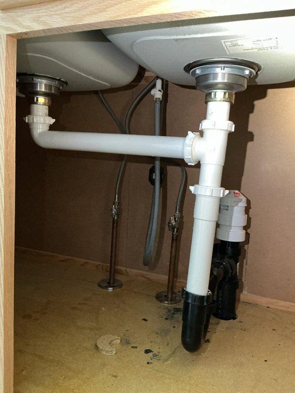 Responded to service call for leak repair in basement of 69-year-old vacant single-family home scheduled for sale. Upon arrival, accessed property and conducted thorough inspection of plumbing systems in basement and crawl space areas.

Discovered extensive corrosion on copper supply lines in crawl space, with significant green-blue patina (verdigris) indicating advanced deterioration. Main horizontal copper pipe exhibited rough, bumpy texture with turquoise discoloration covering substantial section. Blue-handled shutoff valve showed dark staining and corrosion around base and connection points. Secondary diagonal copper pipe also displayed patches of green corrosion consistent with aging plumbing system.

Inspected kitchen sink cabinet area and found double sink drain system with white PVC trap configuration. Examined chrome sink strainers, flexible braided supply lines, and associated drain connections. Noted dark spots on cabinet floor but determined these were pre-existing stains 