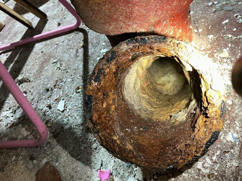 Responded to sewage backup in basement. Upon arrival, found multiple drainage points affected including three basement floor drains and one exterior lawn drain. Conducted diagnostic inspection of the drainage system to identify source of backup.

Visual inspection revealed severely corroded cast iron drain stack with extensive rust deterioration throughout the pipe interior and exterior surfaces. The vertical stack showed advanced corrosion with significant buildup of rust deposits and mineral scaling along interior walls, indicating long-term moisture exposure and structural compromise of the piping material. Concrete floor surrounding the drain exhibited staining consistent with chronic sewage seepage.

Additional inspection of basement drainage system revealed water damage and rust staining on concrete block walls near plumbing configuration, suggesting historical moisture intrusion issues. PVC drainage and venting system observed in upper wall area appeared to be later additions to