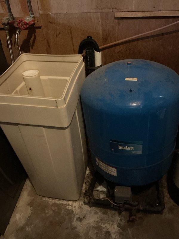 Conducted on-site assessment of existing water heater system in residential basement utility area. Documented current installation including aging water heater with copper piping connections, brass fittings, and associated plumbing infrastructure. Evaluated condition of surrounding equipment including water softener unit and WellSaver pressure tank system. Photographed existing configuration showing top-mounted connections, safety components, and proximity to HVAC ductwork to prepare comprehensive replacement estimate. Noted access considerations and existing plumbing layout for new water heater installation planning.