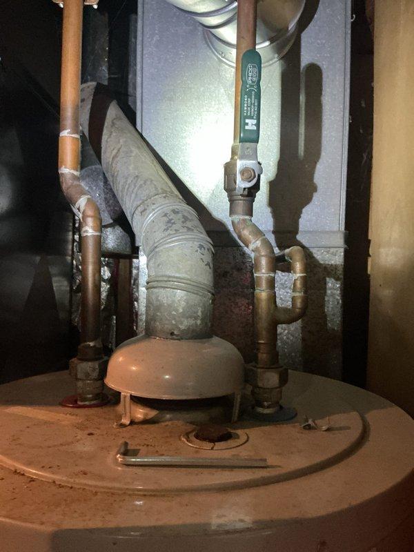 Conducted on-site assessment of existing water heater system in residential basement utility area. Documented current installation including aging water heater with copper piping connections, brass fittings, and associated plumbing infrastructure. Evaluated condition of surrounding equipment including water softener unit and WellSaver pressure tank system. Photographed existing configuration showing top-mounted connections, safety components, and proximity to HVAC ductwork to prepare comprehensive replacement estimate. Noted access considerations and existing plumbing layout for new water heater installation planning.