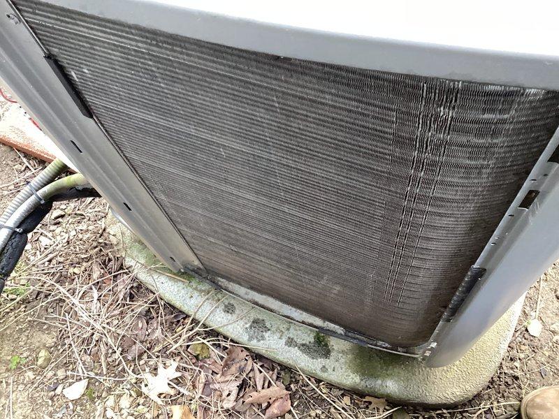 Completed MVP recurring maintenance visit on residential cooling system. Inspected outdoor condenser unit, which showed moderate accumulation of debris in heat exchanger coils with visible discoloration and dirt buildup between fin rows. Unit operational with fan assembly and protective grilles intact. Noted environmental debris around base including leaves and organic matter on surrounding soil. Condenser pad exhibited minor weathering and surface growth consistent with age. All major components visually confirmed functional during inspection.