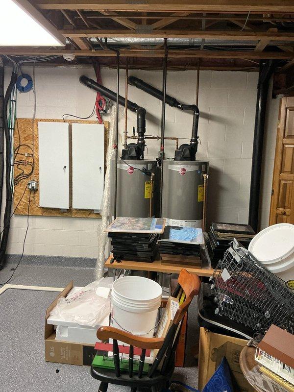 Responded to service call for potential water heater replacement in a fifteen-year-old residence. Upon arrival, inspected existing dual water heater installation in basement utility area. Documented current plumbing configuration including copper pipe connections, shut-off valves, and water treatment components. Assessed condition of both gray cylindrical water heaters mounted on concrete block wall, noting connection points, valve accessibility, and overall system layout. Photographed existing installation including supply and discharge piping, electrical connections, and surrounding utility space to provide comprehensive documentation for replacement estimate.