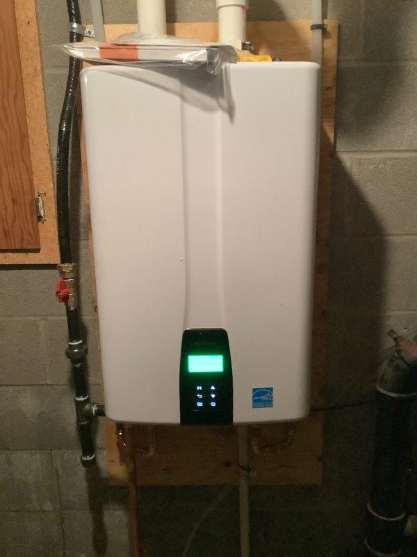 Completed installation of Navien tankless water heater unit in basement utility area. Mounted unit securely to concrete block wall and connected all necessary plumbing lines including hot and cold water supply pipes with proper insulation. Installed PVC venting system from top of unit, integrated copper piping with shutoff valves, and verified all connections for proper seal and operation. Unit powered on successfully with digital display functioning and showing operational status, confirming system is ready for use.