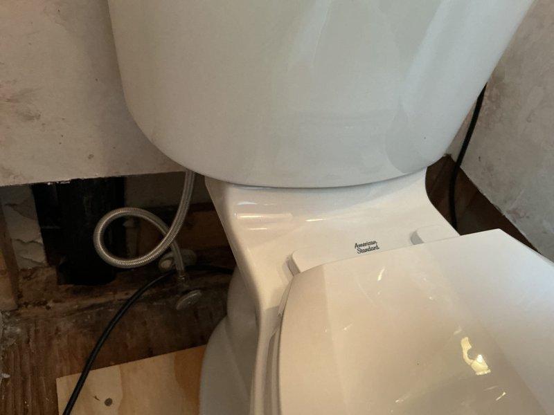 Removed existing round bowl toilet and replaced with American Standard Champion elongated bowl model, upgraded to chair height configuration at 16.5 inches for improved accessibility. Installation completed on plywood subfloor in bathroom undergoing renovation, with new water supply line connected and all plumbing connections secured and tested for proper operation.